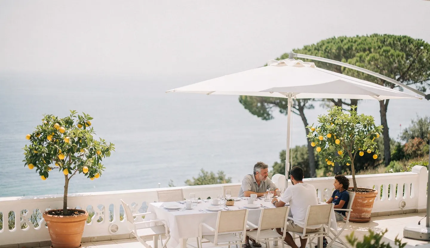 A table laid on a terrace above the sea, under a white parasol.
